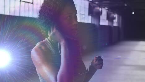 Animation-of-glowing-light-over-woman-putting-earphones-on-before-workout-in-gym