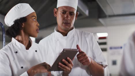 Two-diverse-male-and-female-chefs-talking-and-using-tablet-in-restaurant-kitchen