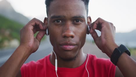 Portrait-of-african-american-man-wearing-earphones-while-standing-on-the-road