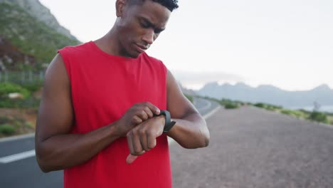 African-american-man-using-fitness-band-while-standing-on-the-road