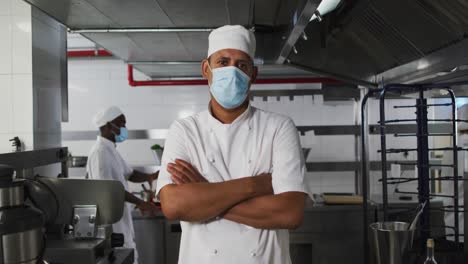 Portrait-of-mixed-race-male-chef-wearing-face-mask-with-arms-crossed