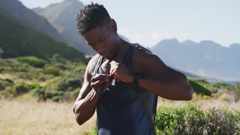 African-american-man-exercising-outdoors-putting-backpack-on-in-countryside-on-a-mountain