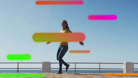 Animation-of-floating-colourful-shapes-over-woman-dancing-on-promenade-by-the-sea