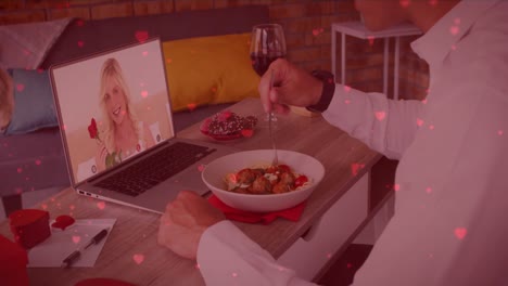 Red-heart-icons-floating-over-caucasian-man-having-lunch-while-having-a-video-call-on-laptop