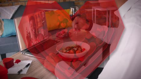 Rotes-Herz-Schlägt-über-Kaukasischem-Mann,-Der-Zu-Mittag-Isst,-Während-Er-Einen-Videoanruf-Auf-Dem-Laptop-Führt