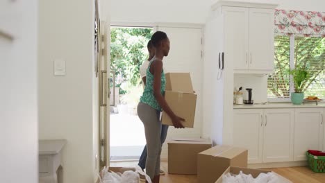 Happy-african-american-couple-walking-into-house-carrying-packing-boxes