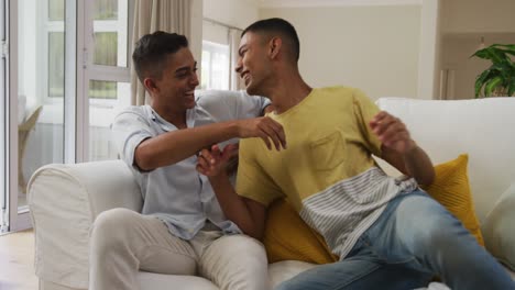 Smiling-mixed-race-gay-male-couple-hugging-on-sofa