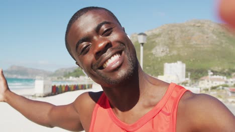 Retrato-De-Un-Hombre-Afroamericano-Sonriente,-Hablando-Y-Mostrando-El-Mar,-Tomando-Un-Descanso-En-El-Ejercicio-Al-Aire-Libre