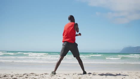 African-american-man-stretching-on-the-beach,-exercising-outdoors-by-the-sea