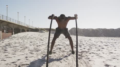 African-american-man-exercising-with-battling-ropes-outdoors-on-the-beach