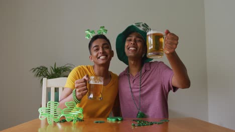 Mixed-race-gay-male-couple-making-st-patrick's-day-video-call-raising-glasses-wearing-costumes
