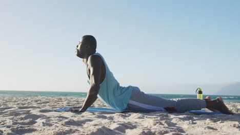 Focused-african-american-man-practicing-yoga-on-beach,-exercising-outdoors-by-the-sea