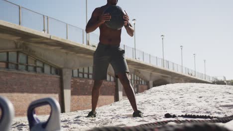 Fokussierter-Afroamerikanischer-Mann,-Der-Den-Ball-Hebt-Und-Draußen-Am-Strand-Trainiert