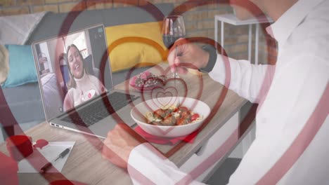 Concentric-red-hearts-over-caucasian-man-having-lunch-while-having-a-video-call-on-laptop