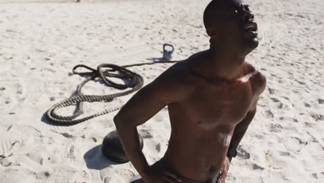 Tired-african-american-man-taking-break-in-exercise-outdoors-on-beach