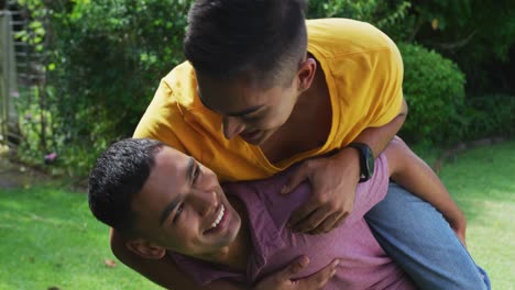 Smiling-mixed-race-gay-male-couple-having-fun-piggybacking-in-garden
