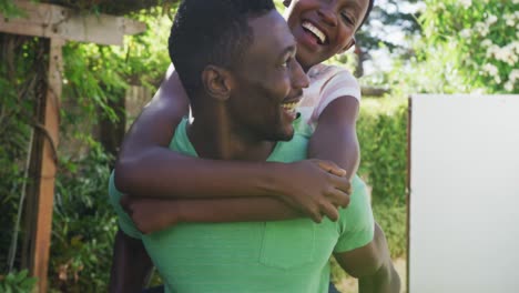 Glückliches-Afroamerikanisches-Paar,-Das-Spaß-Beim-Huckepackfahren-Im-Sonnigen-Garten-Hat-Und-Lächelt