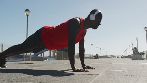 Focused-african-american-man-doing-press-ups,-exercising-outdoors-by-the-seaside