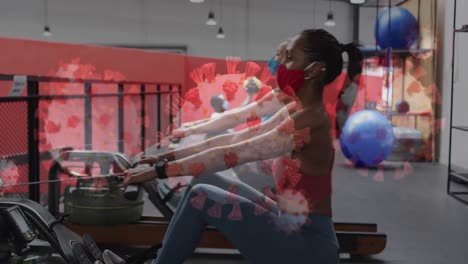 Covid-19-cells-floating-against-two-diverse-woman-wearing-face-mask-working-out-at-the-gym