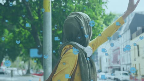 Multiple-digital-icons-floating-against-woman-wearing-hijab-hailing-a-taxi-on-the-street