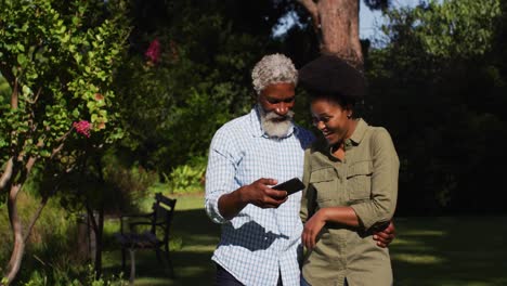 Lächelndes-Afroamerikanisches-Seniorenpaar,-Das-Sich-Im-Sonnigen-Garten-Unterhält-Und-Ein-Selfie-Macht