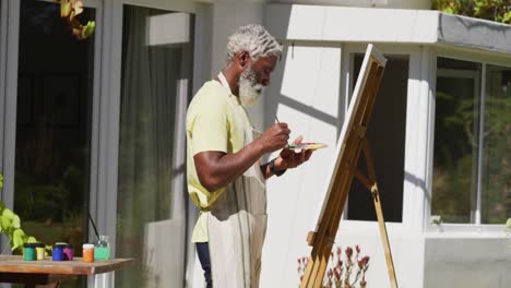 Senior-african-american-man-painting-picture-on-a-canvas-in-sunny-garden