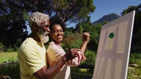 Smiling-african-american-couple-talking-in-sunny-garden-woman-painting-picture-on-a-canvas