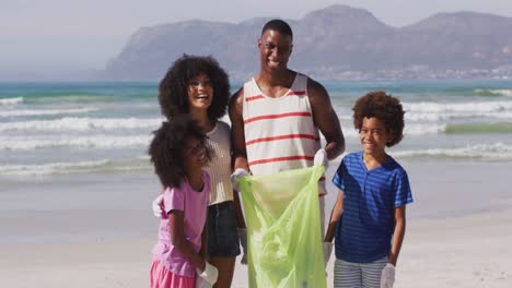 Porträt-Afroamerikanischer-Eltern-Mit-Ihren-Kindern,-Die-Müll-Und-Flaschen-Am-Strand-Sammeln