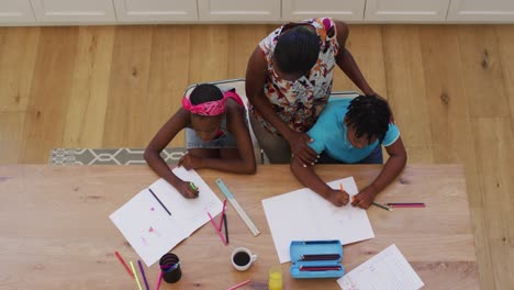 Overhead-view-of-african-american-mother-helping-her-daughter-and-son-with-homework-at-home