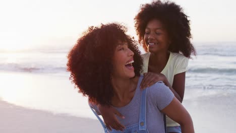 Afroamerikanische-Mutter,-Die-Ihrer-Tochter-Am-Strand-Eine-Huckepackfahrt-Gibt