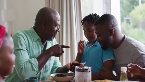 African-american-grandfather,-father-and-son-smiling-while-using-smartphone-together-at-home