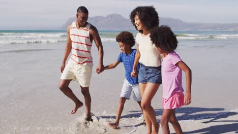 Padres-Afroamericanos-Sonrientes-Y-Sus-Hijos-Caminando-Y-Tomados-De-La-Mano-En-La-Playa.