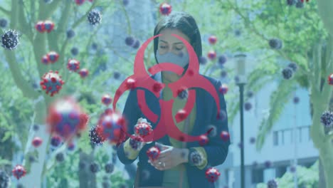 Animation-of-biohazard-symbol-and-covid-19-cells-over-woman-using-smartphone-wearing-face-mask