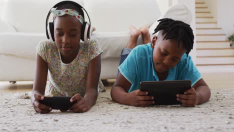 African-american-brother-and-sister-using-electronic-devices-lying-on-the-floor-at-home