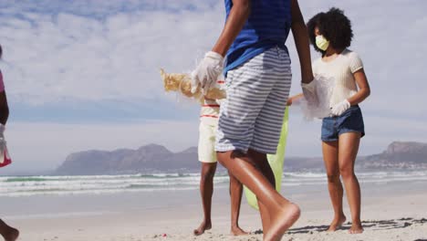 Afroamerikanische-Eltern-Mit-Zwei-Kindern,-Die-Gesichtsmasken-Tragen,-Sammeln-Müll-Vom-Strand