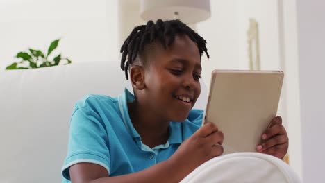 Niño-Afroamericano-Sonriendo-Mientras-Usa-Una-Tableta-Digital-Sentado-En-El-Sofá-En-Casa