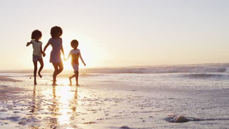 Afroamerikanische-Mutter,-Sohn-Und-Tochter-Haben-Spaß-Beim-Gemeinsamen-Spaziergang-Bei-Sonnenuntergang-Am-Strand