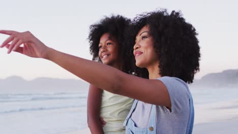 African-american-mother-and-daughter-smiling-looking-at-each-other-at-the-beach