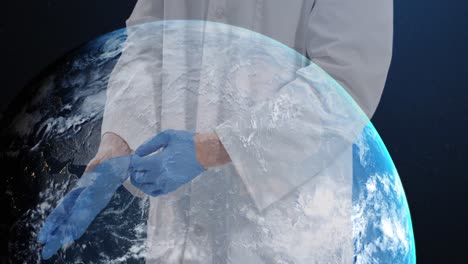 Mid-section-of-male-doctor-wearing-surgical-gloves-against-globe-spinning-on-blue-background