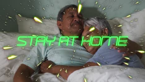 Animation-of-stay-at-home-text-over-senior-couple-cuddling-in-bed