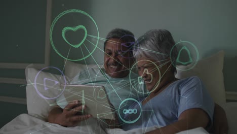 Animation-of-network-of-connections-with-icons-over-senior-couple-using-tablet-in-bed-at-home