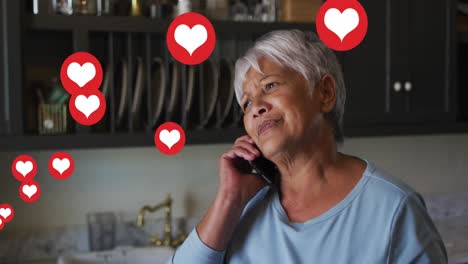 Multiple-heart-icons-floating-against-african-american-senior-woman-talking-on-smartphone