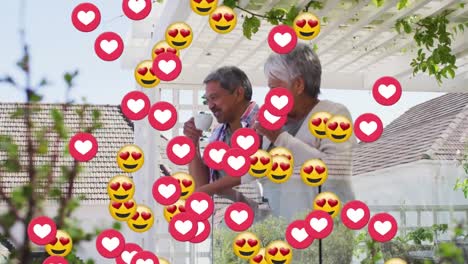Animation-of-emoji-heart-icons-over-senior-couple-drinking-wine-on-balcony