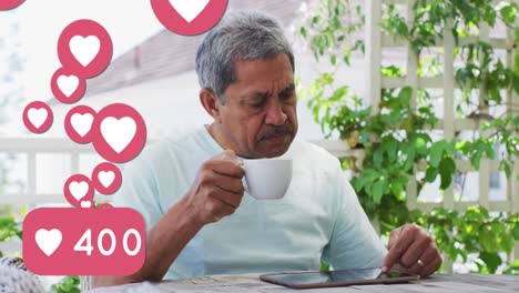 Animation-Von-Herzliebessymbolen-über-Einem-älteren-Mann,-Der-Ein-Tablet-Benutzt-Und-Zu-Hause-Kaffee-Trinkt