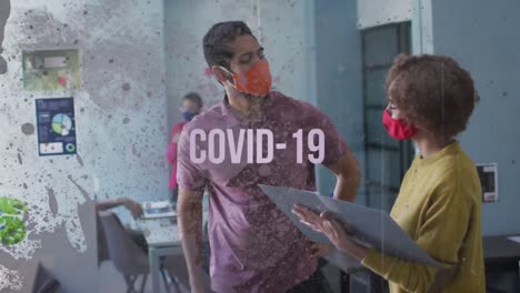 Covid-19-text-against-male-and-female-office-colleague-wearing-face-mask-discussing-at-office