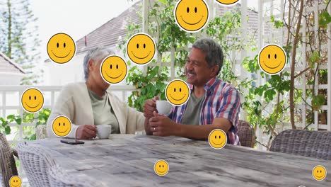 Animation-of-smiling-emojis-over-senior-couple-drinking-coffee-at-home