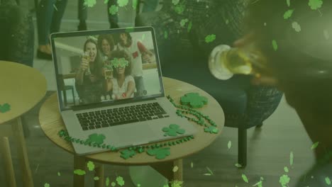 Clover-leaves-falling-against-woman-drinking-beer-while-having-a-video-call-on-laptop-at-a-bar