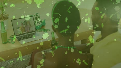 Clover-leaves-falling-against-couple-holding-beers-having-video-call-on-laptop-at-home