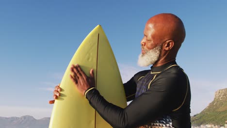 Älterer-Afroamerikanischer-Mann,-Der-Mit-Einem-Surfbrett-Am-Strand-Spaziert