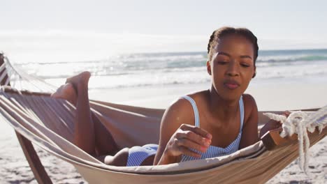 Mujer-Afroamericana-Usando-Una-Tableta-Digital-Mientras-Está-Acostada-En-Una-Hamaca-En-La-Playa